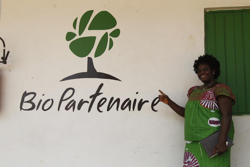 Woman cocoa farmer in front of BioPartenaire Logo